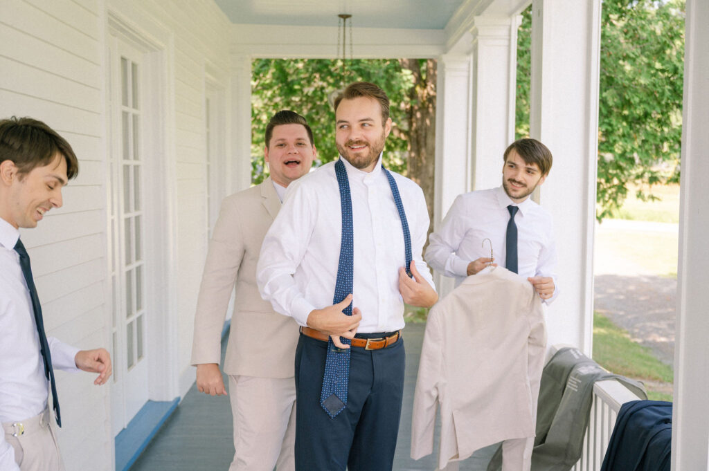 The groom adjusts his tie on the porch of The White House on the Lake while his groomsmen help with final details before the ceremony.