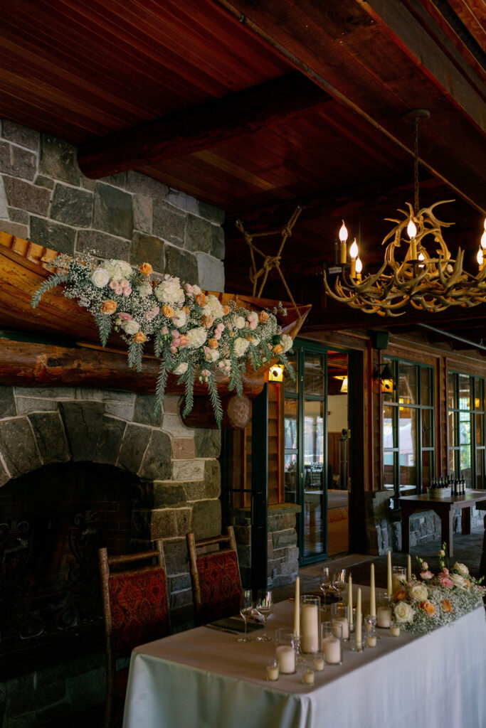 Floral arrangement displayed above a stone fireplace at the Whiteface Lodge, featuring soft blush and white blooms with greenery in an Adirondack lodge interior.
