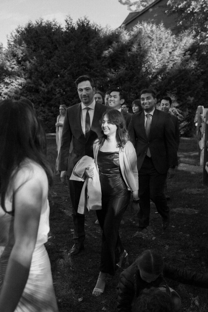 Wedding guests walk toward the ceremony site during a lakeside fall wedding in Lake Placid, captured in black and white.