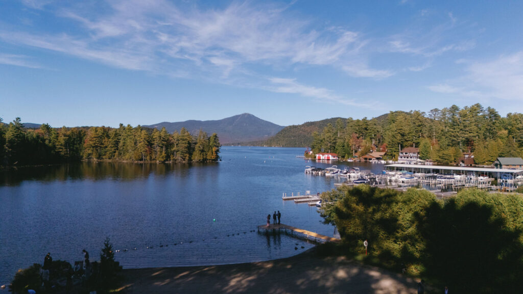 Scenic view of Lake Placid with mountain backdrop and lakeside docks on a clear fall day, captured near the Whiteface Lodge.