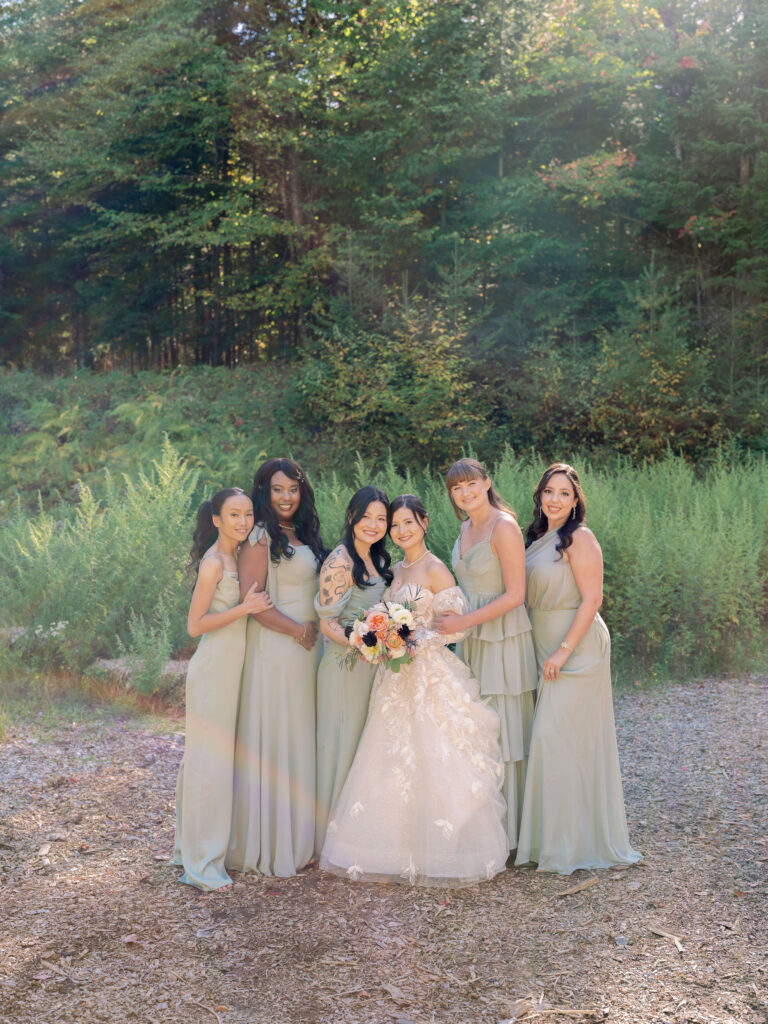 Bride stands with her bridesmaids during fall wedding portraits, surrounded by greenery and soft afternoon light.