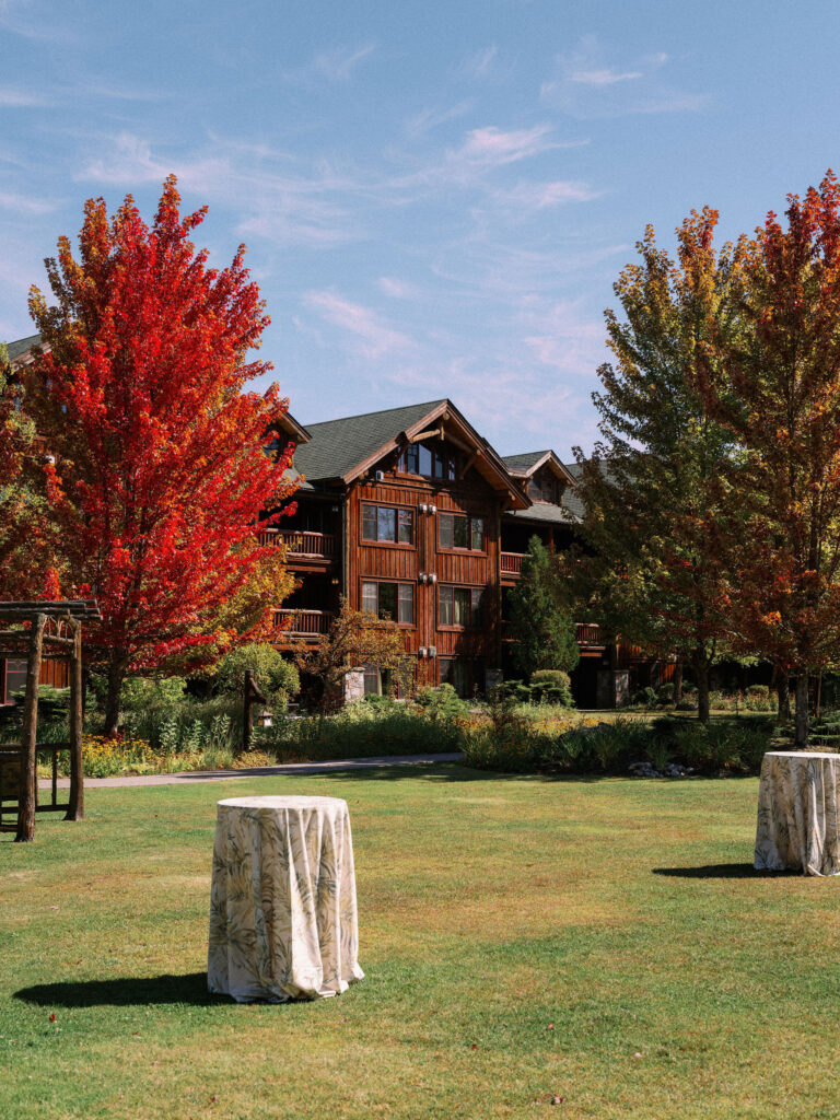 Exterior of the Whiteface Lodge surrounded by vibrant fall foliage and a manicured lawn set for a wedding celebration in Lake Placid, New York.