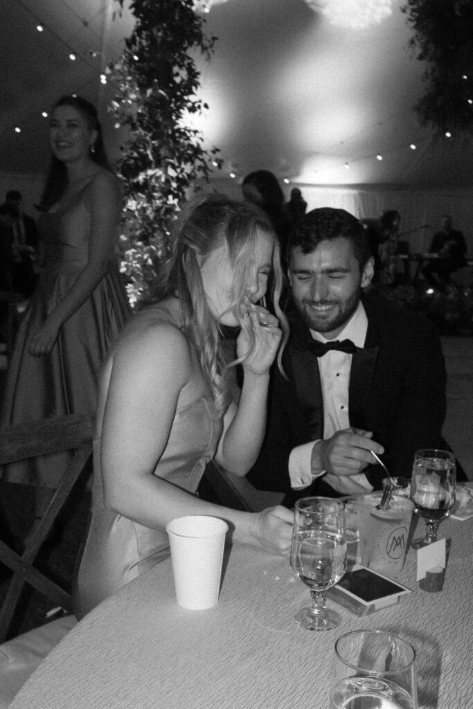 Two guests laugh together at a reception table with drinks during a Lake Placid wedding.