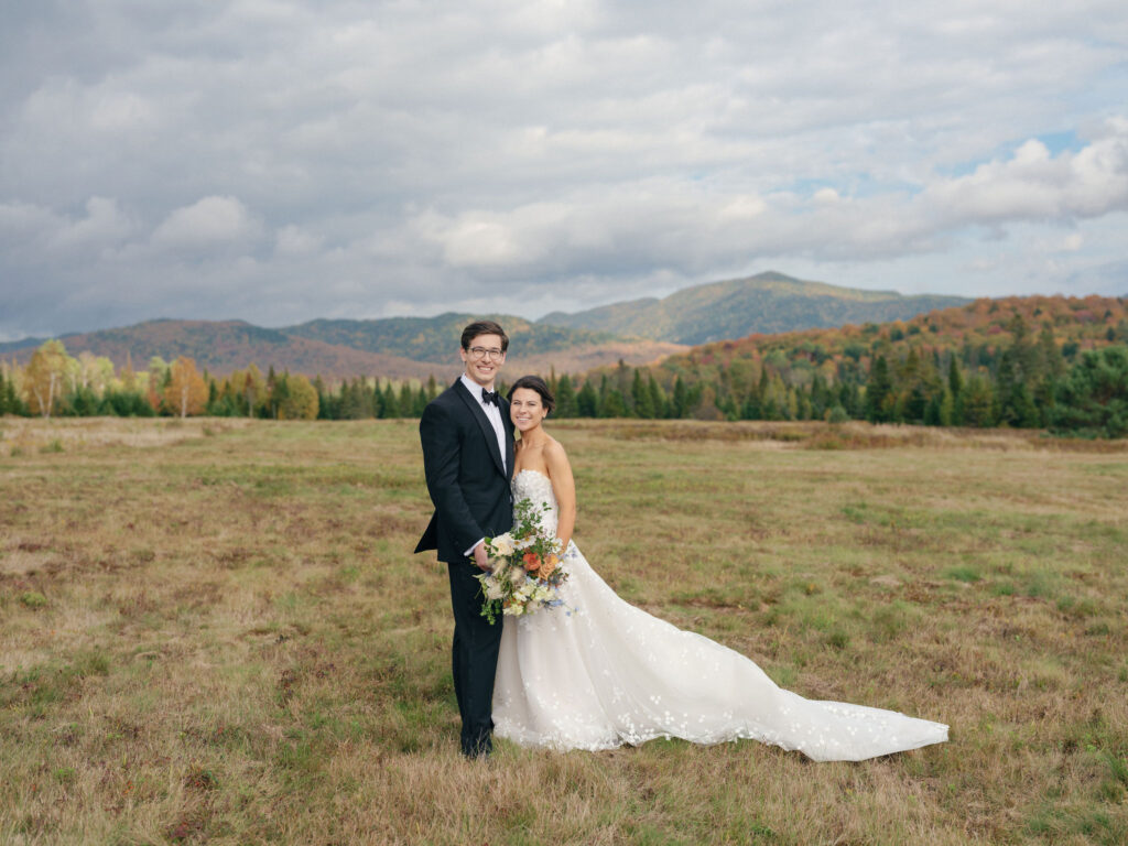 Bride and groom pose together in a mountain field at a private Lake Placid estate with fall Adirondack scenery in the background.