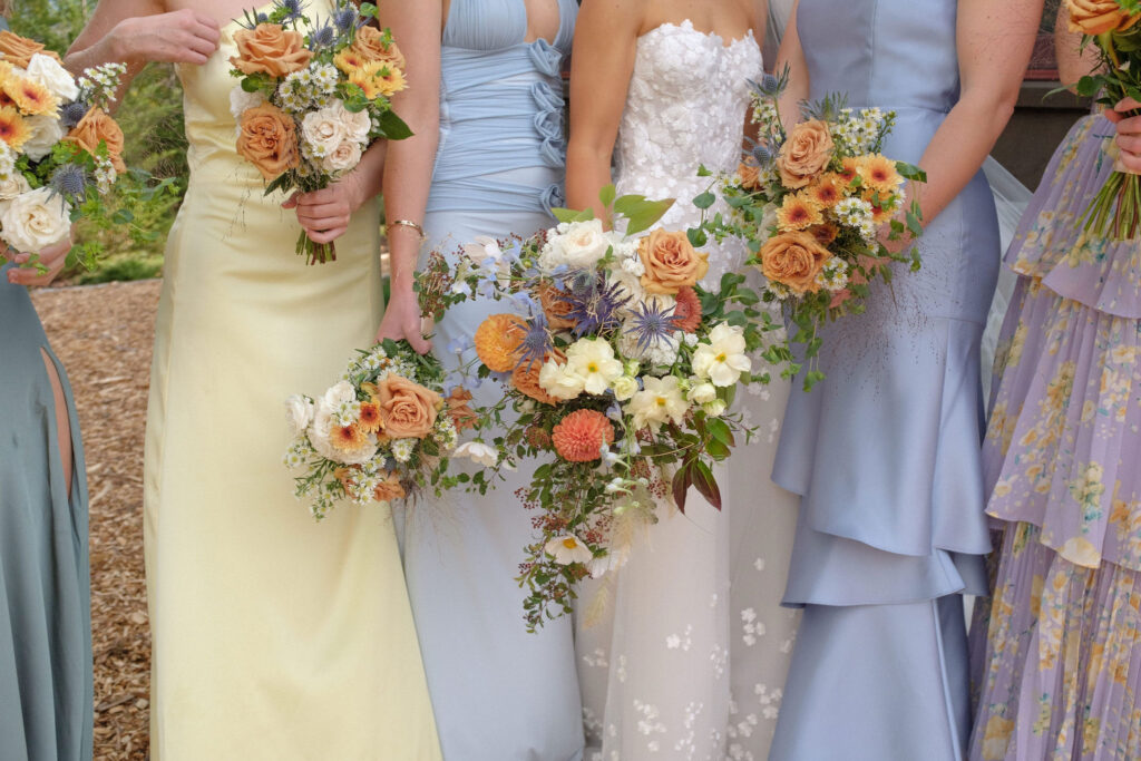 Bridesmaids in pastel dresses hold colorful garden-style bouquets with roses, daisies, and wildflowers at a Lake Placid wedding in the Adirondacks.
