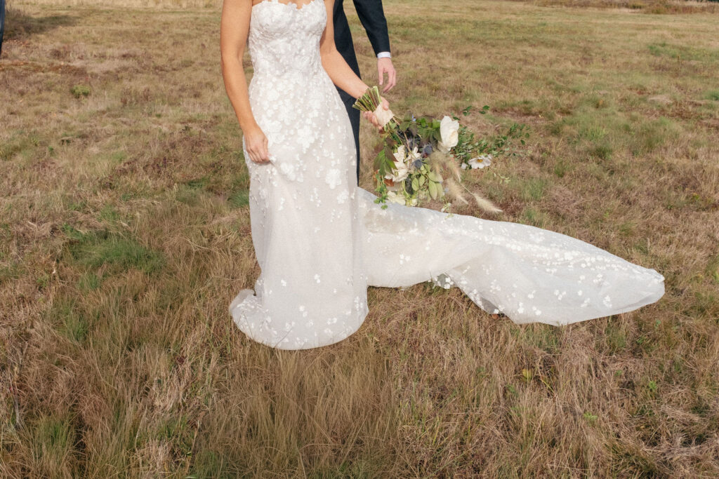 Close-up of a bride’s lace wedding dress and bouquet with soft florals and greenery during a Lake Placid outdoor wedding.