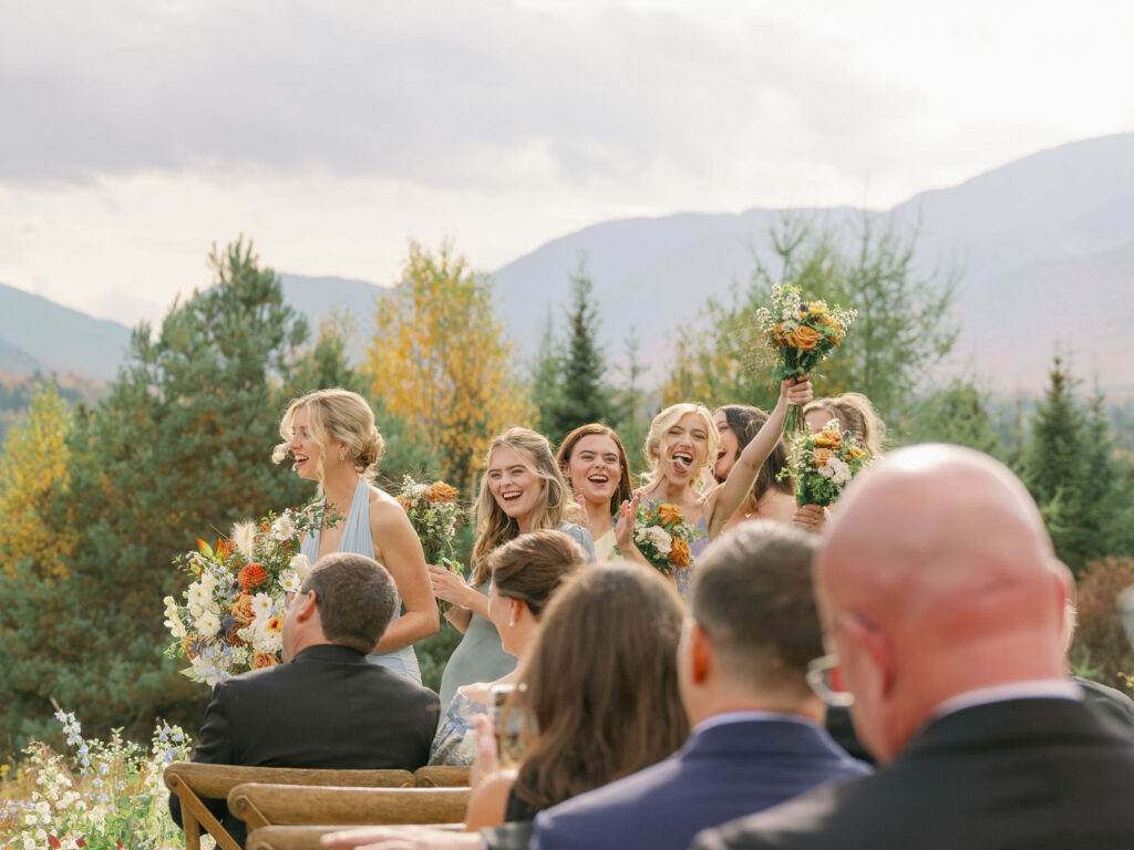 Bridesmaids cheer and laugh during an outdoor wedding ceremony at a private estate in Lake Placid, New York, with Adirondack mountains and fall foliage in the background.