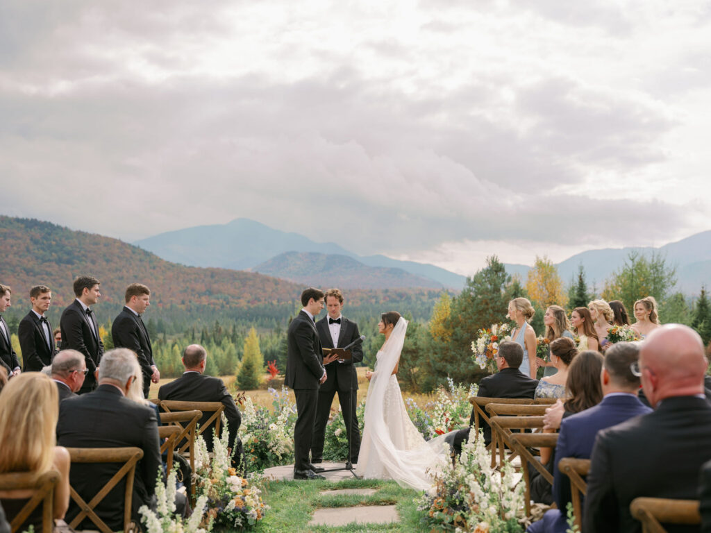 Bride and groom stand at the altar during an outdoor wedding ceremony in Lake Placid, New York, surrounded by guests and mountain views in the Adirondacks.