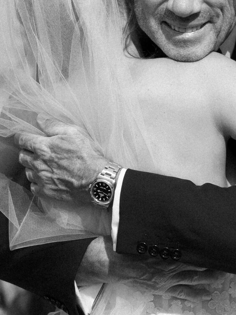 Black and white close-up of a father holding his daughter’s arm during a wedding ceremony, highlighting emotional connection and intimate detail.