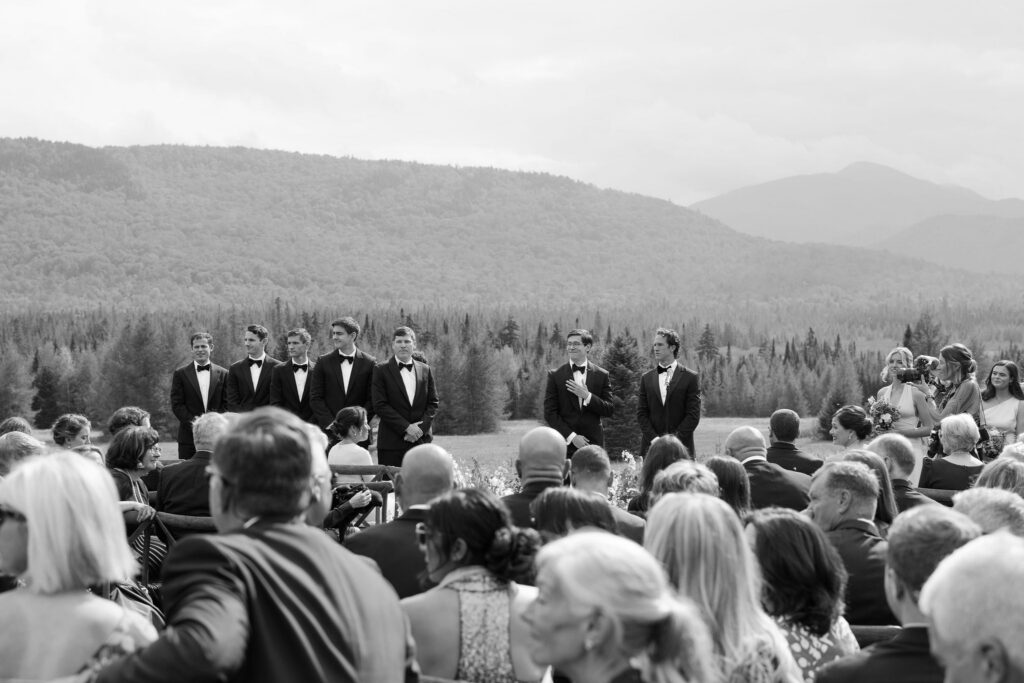 Black and white image of a groom reacting during the ceremony as guests look on, capturing a candid emotional moment in the Adirondacks.