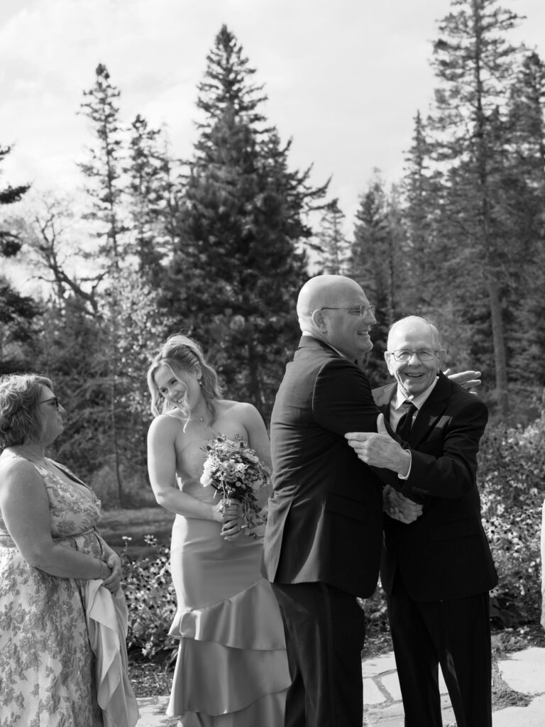 Wedding guests smile and embrace during an outdoor ceremony at a private estate in Lake Placid, New York, surrounded by forest.
