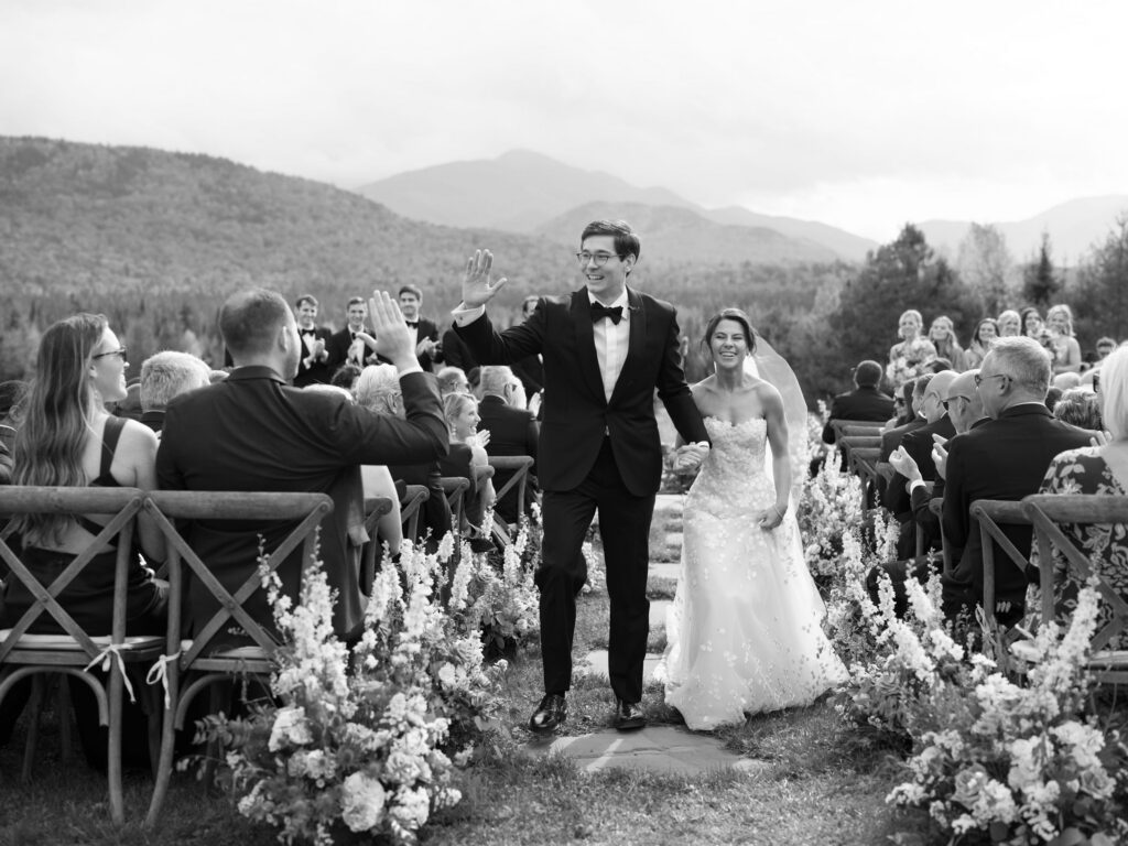 Bride and groom walk down the aisle smiling and high-fiving guests after their outdoor wedding ceremony in Lake Placid, New York.