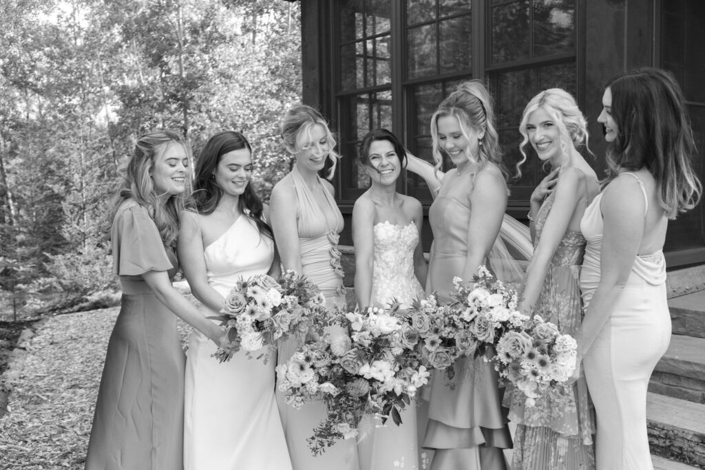 Bride and bridesmaids laugh together while holding bouquets outside a private estate wedding in Lake Placid, New York.