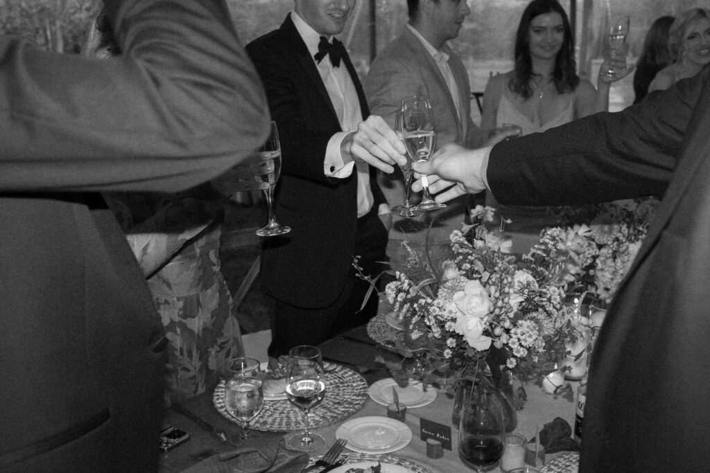 Guests clink champagne glasses over a floral centerpiece during reception at a Lake Placid wedding.