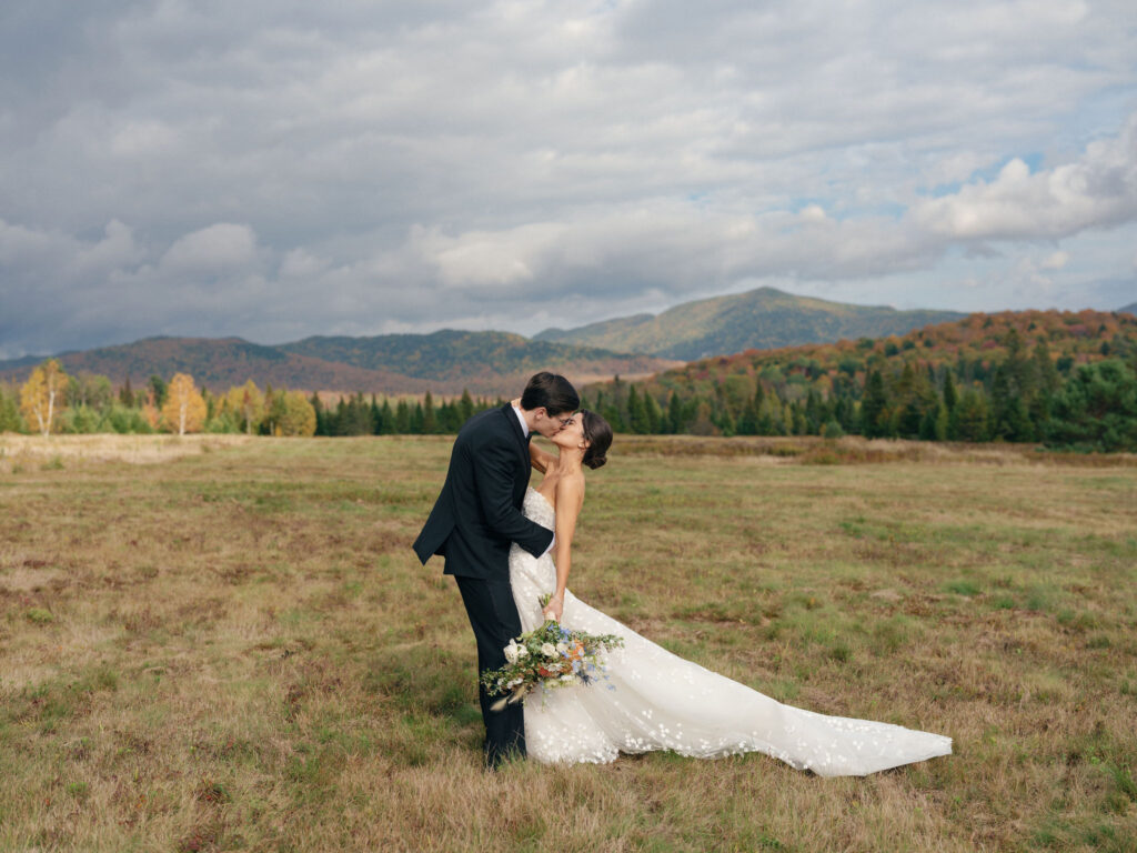 Bride and groom share a kiss in an open Adirondack field during their Lake Placid, New York wedding portraits.