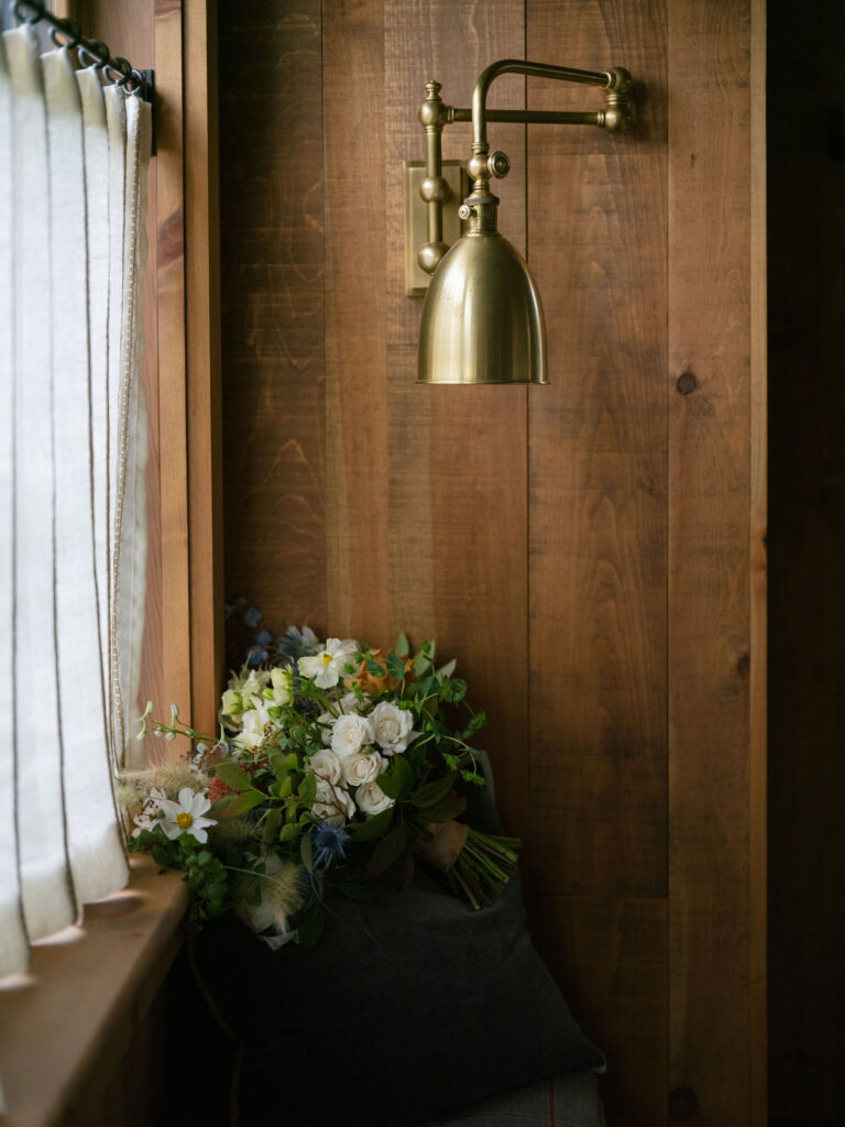 Bridal bouquet resting by window under brass light fixture at a Lake Placid private estate wedding