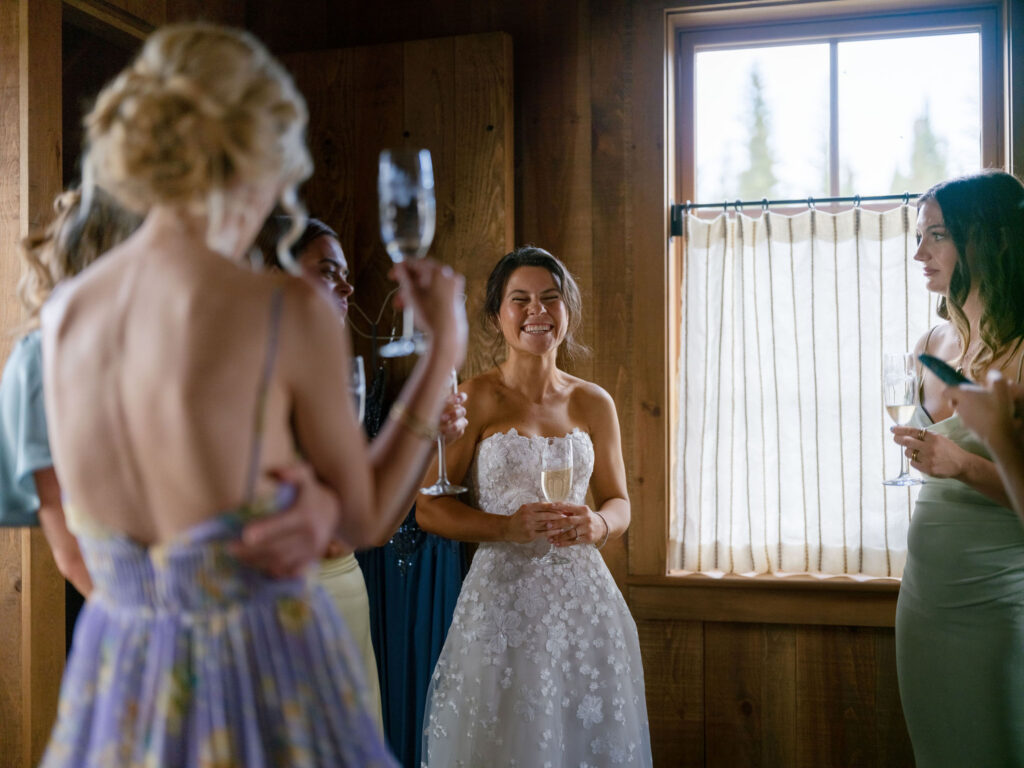 Bride laughing with bridesmaids by window light inside cabin during a Lake Placid private estate wedding