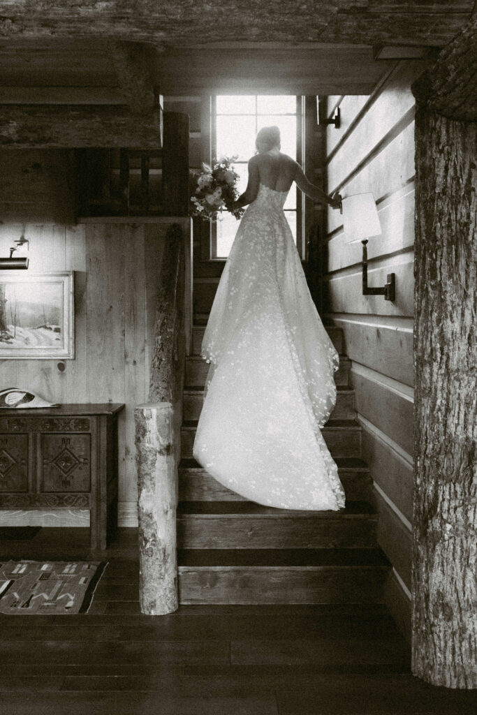 Bride walking upstairs with bouquet in a rustic cabin during a Lake Placid private estate wedding