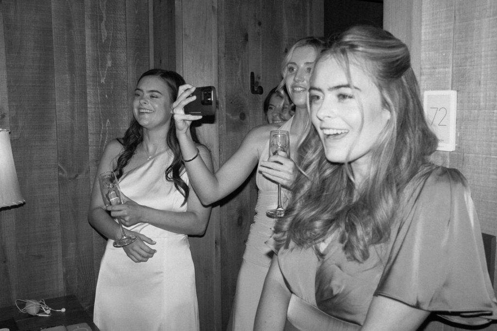 Bridesmaids laughing and toasting with champagne inside Adirondack cabin during a Lake Placid private estate wedding