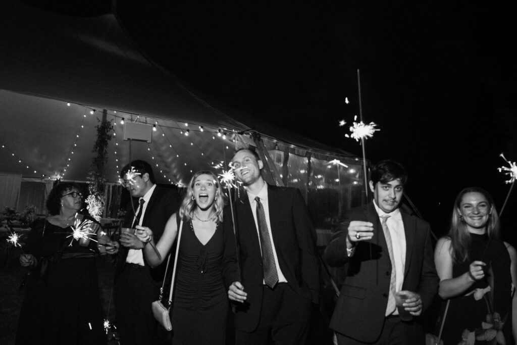 Guests line up holding sparklers outside a sailcloth tent for a wedding send-off in Lake Placid.