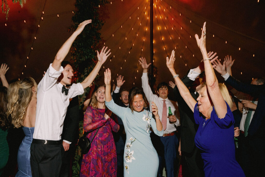 Wedding guests raise their hands and dance under warm string lights during a lively reception in Lake Placid.