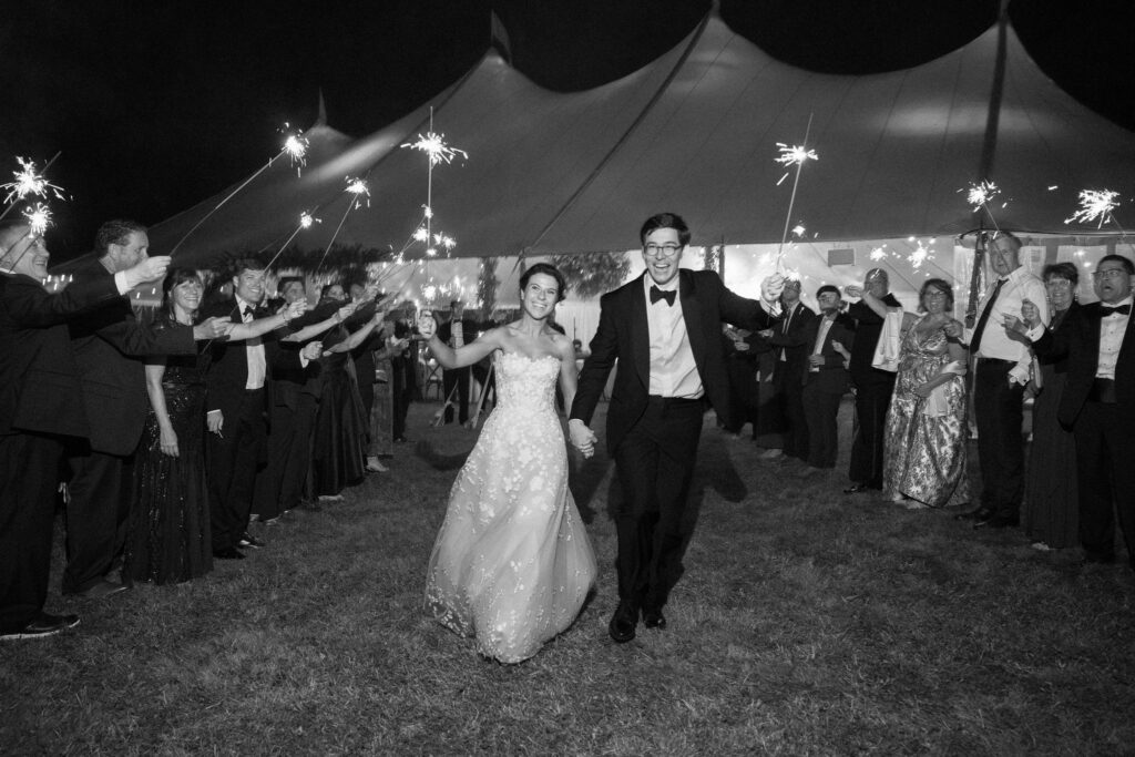Bride and groom run through a tunnel of sparklers held by guests outside a tented wedding in Lake Placid, New York.