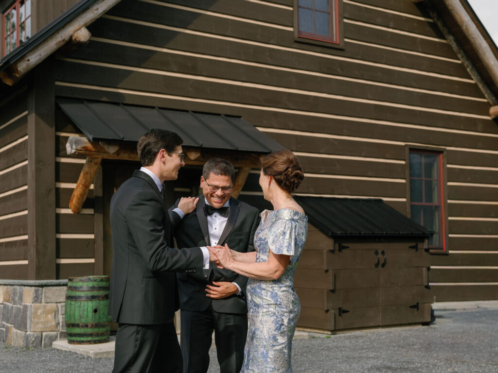 Groom shares a joyful moment with family members outside a rustic Adirondack estate during a Lake Placid wedding day.
