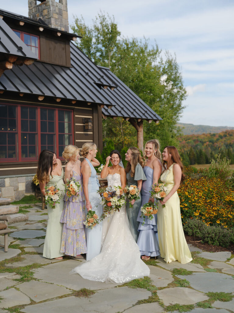 Bride and bridesmaids stand together in pastel dresses holding bouquets outside a Lake Placid private estate with mountain views.