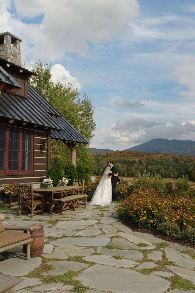 Bride and groom embrace on a stone patio overlooking Adirondack mountains during a private estate wedding in Lake Placid, New York.