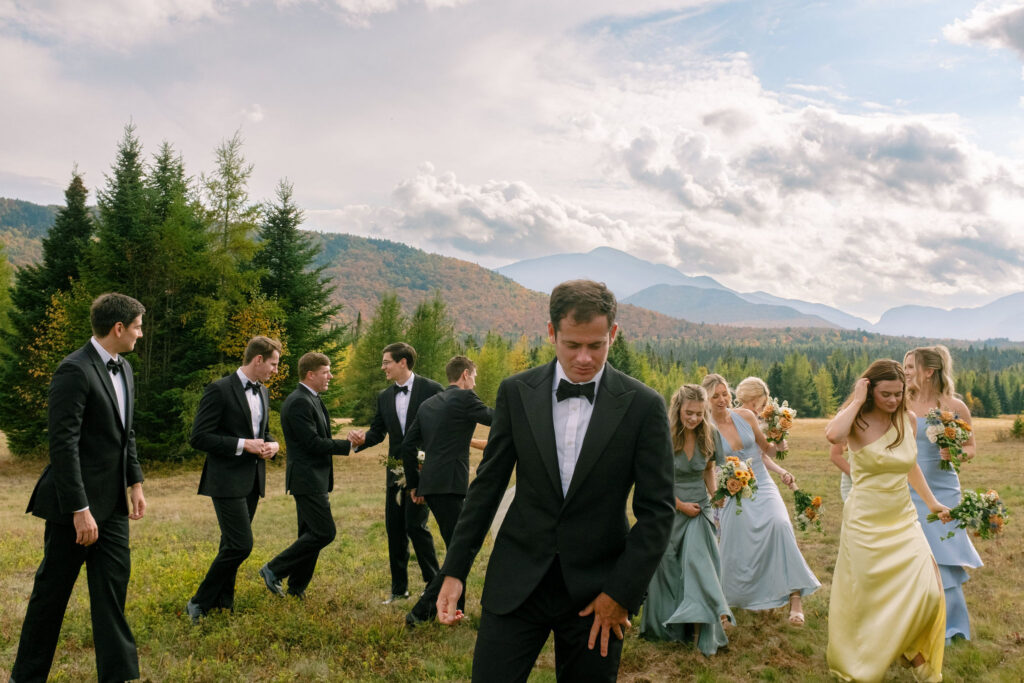 Bridesmaids and groomsmen move and laugh together in a field during a candid moment at a Lake Placid, New York wedding.