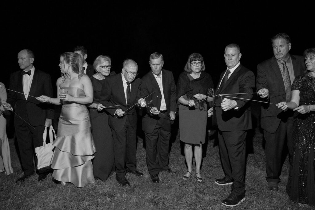 Wedding guests light sparklers in a line outside during a nighttime reception in Lake Placid, New York.