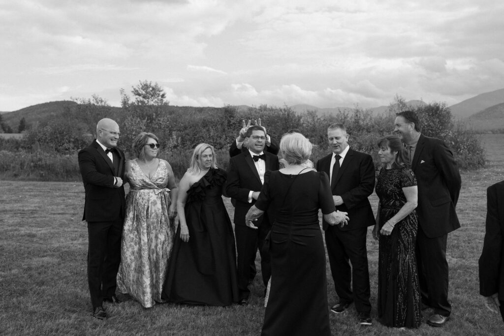 Wedding guests laugh as someone playfully gives bunny ears during cocktail hour at a Lake Placid, New York wedding.