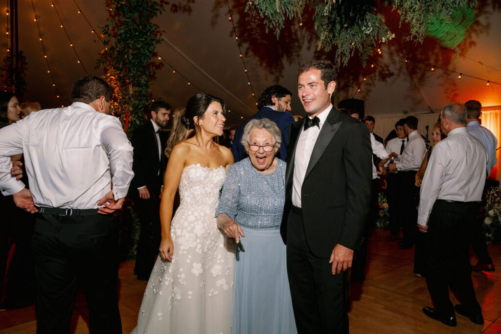 Bride and groom smile with an excited grandmother on the dance floor during a Lake Placid wedding reception.