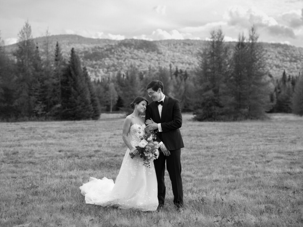 Bride and groom stand together in an open field with Adirondack mountains behind them during a Lake Placid wedding.