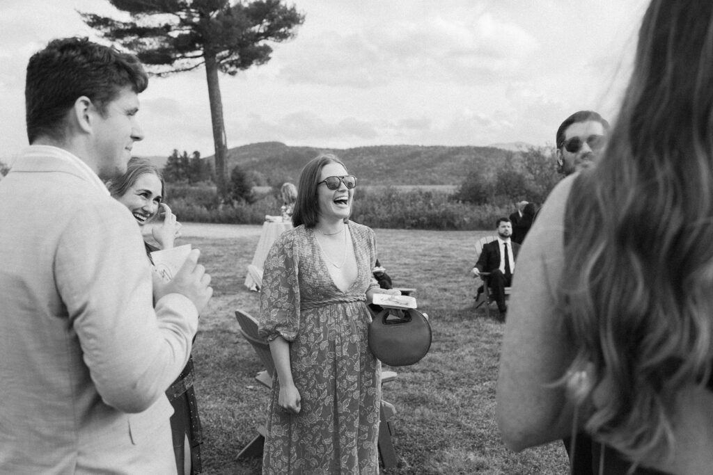 Wedding guests laugh and mingle during outdoor cocktail hour with Adirondack mountain views in Lake Placid, New York.