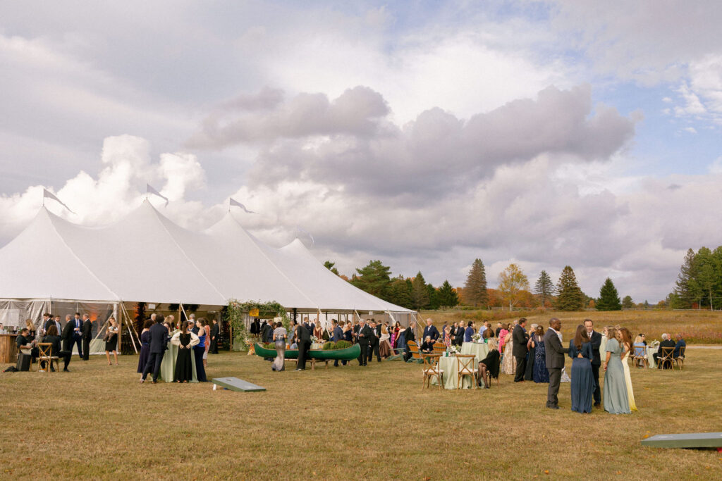 Guests gather outside a sailcloth tent during cocktail hour at a private estate wedding in Lake Placid, New York.