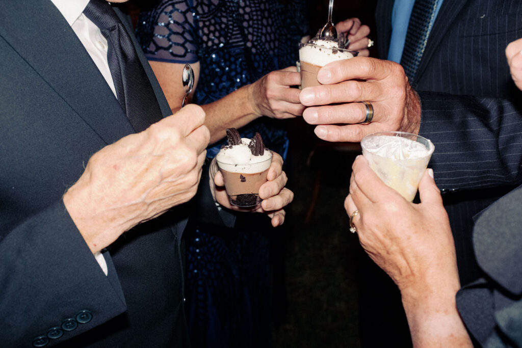 Wedding guests hold chocolate dessert cups and cocktails during a lively reception at River Ranch in Lake Placid, New York.