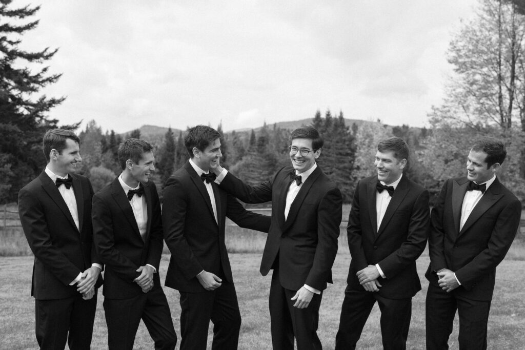 Groomsmen laughing together in tuxedos outdoors at River Ranch Lake Placid wedding