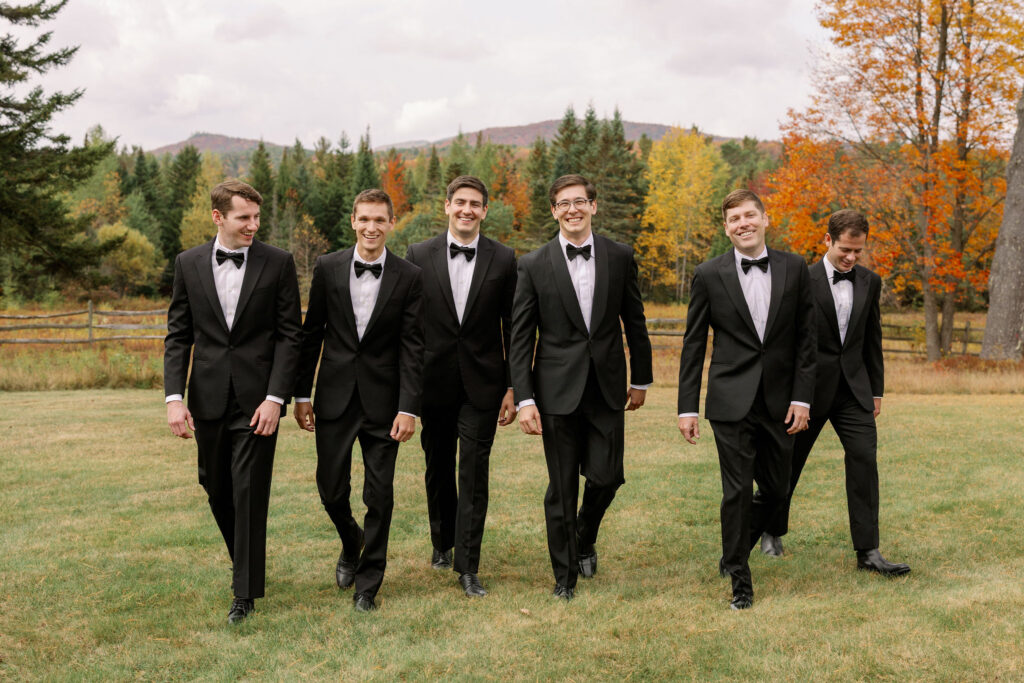 Groomsmen walking together across field with Adirondack fall foliage at River Ranch Lake Placid wedding