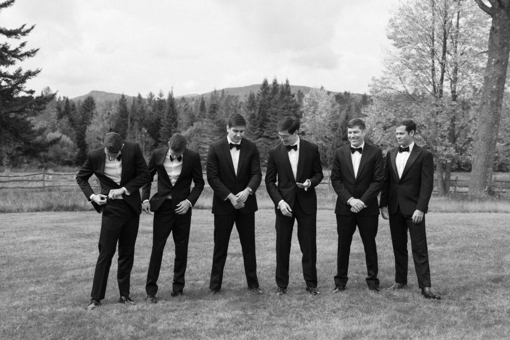 Groomsmen adjusting suits and laughing outdoors at River Ranch Lake Placid wedding