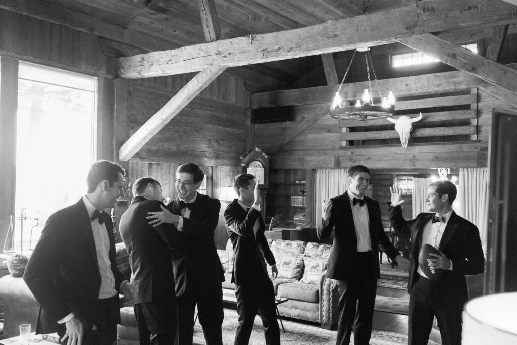 Groomsmen cheering and celebrating inside rustic cabin at River Ranch Lake Placid wedding with football and natural window light