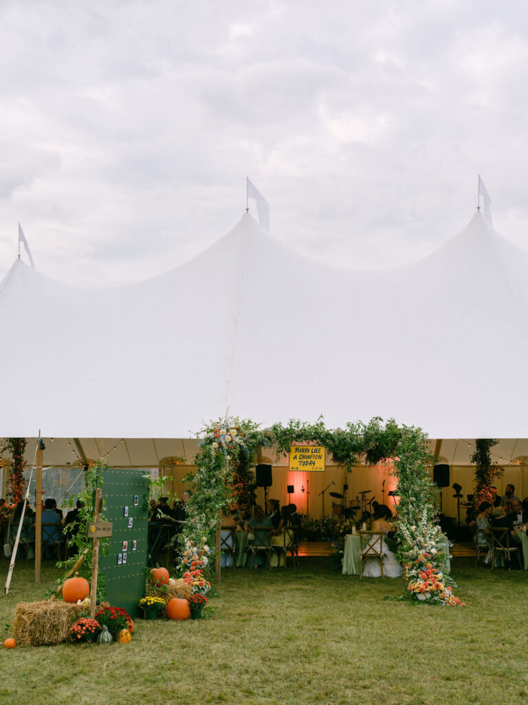 Floral-covered entrance to a sailcloth reception tent with pumpkins and fall decor at a Lake Placid, New York wedding.