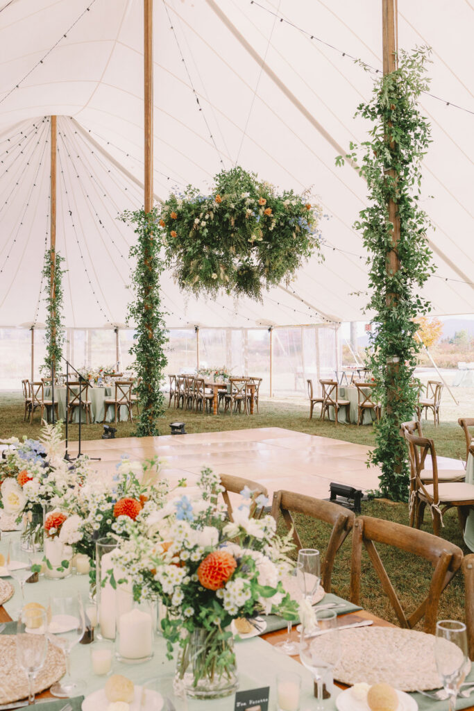 Reception setup inside a sailcloth tent with greenery-wrapped poles, floral centerpieces, and a dance floor at a Lake Placid wedding