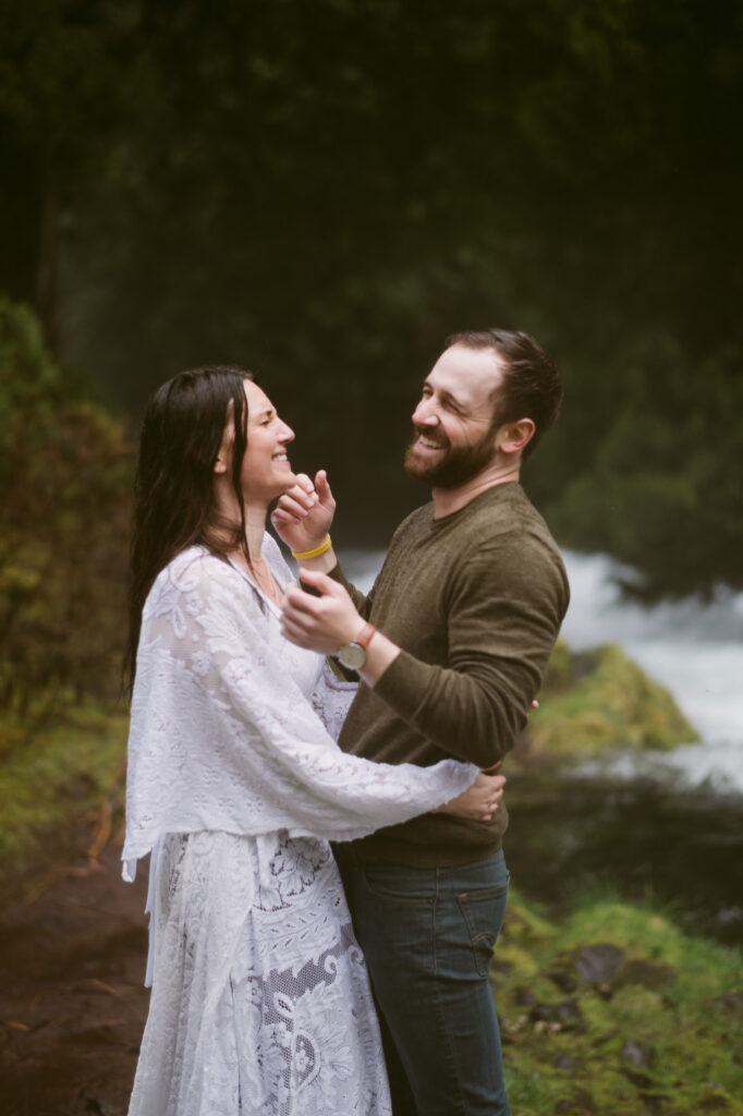 A bride and groom hold each other close while laughing at Sahalie Falls in Oregon.