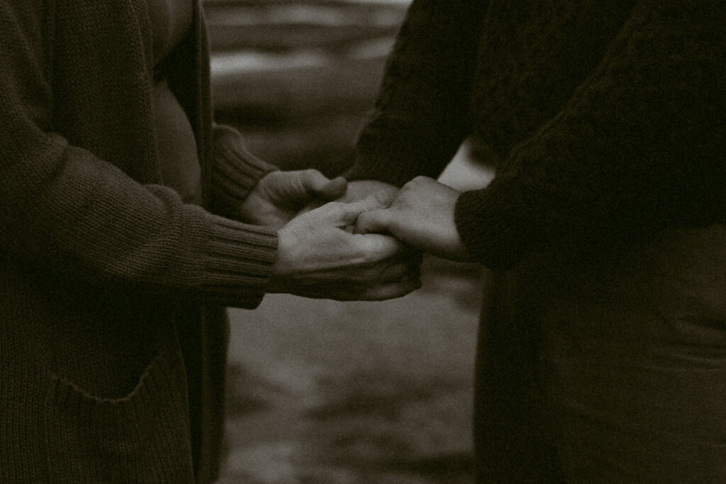 A black and white close-up image of two people holding hands.