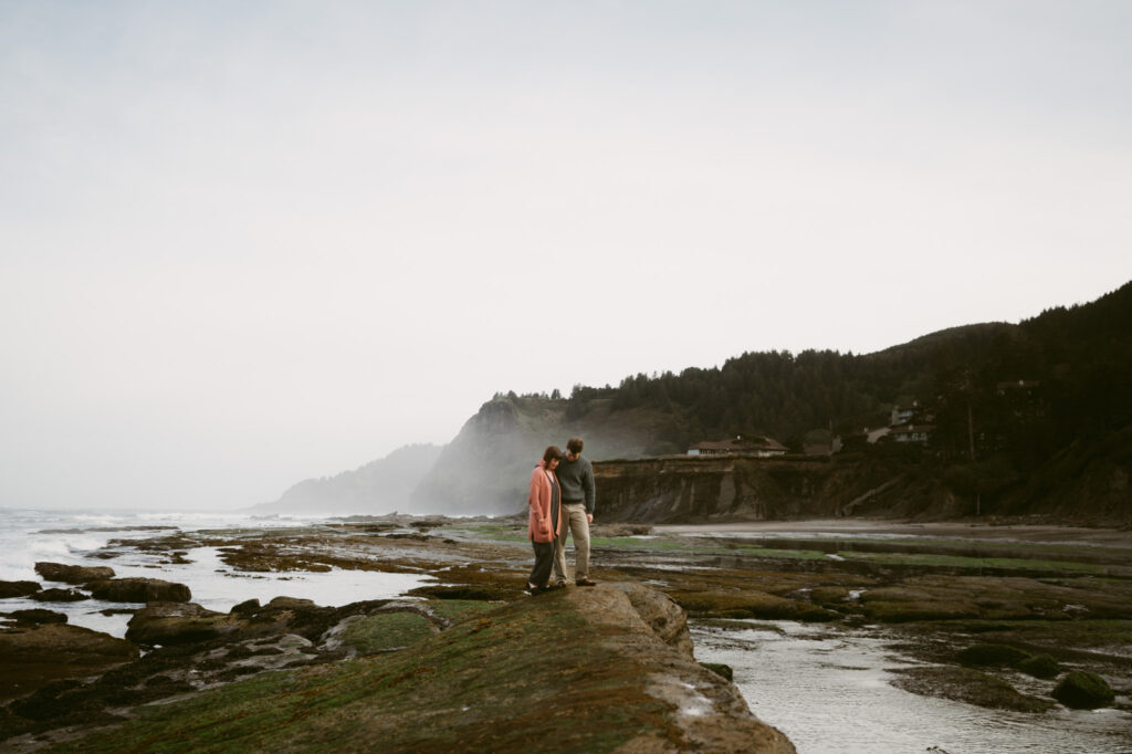A far away photo of a man and woman walking along the rocks at Otter Crest Beach in Oregon.