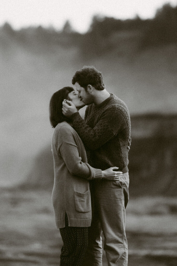 A black and white image of a man and woman kissing. The woman's hands are on the man's waist and his hands are gently cupping her face.