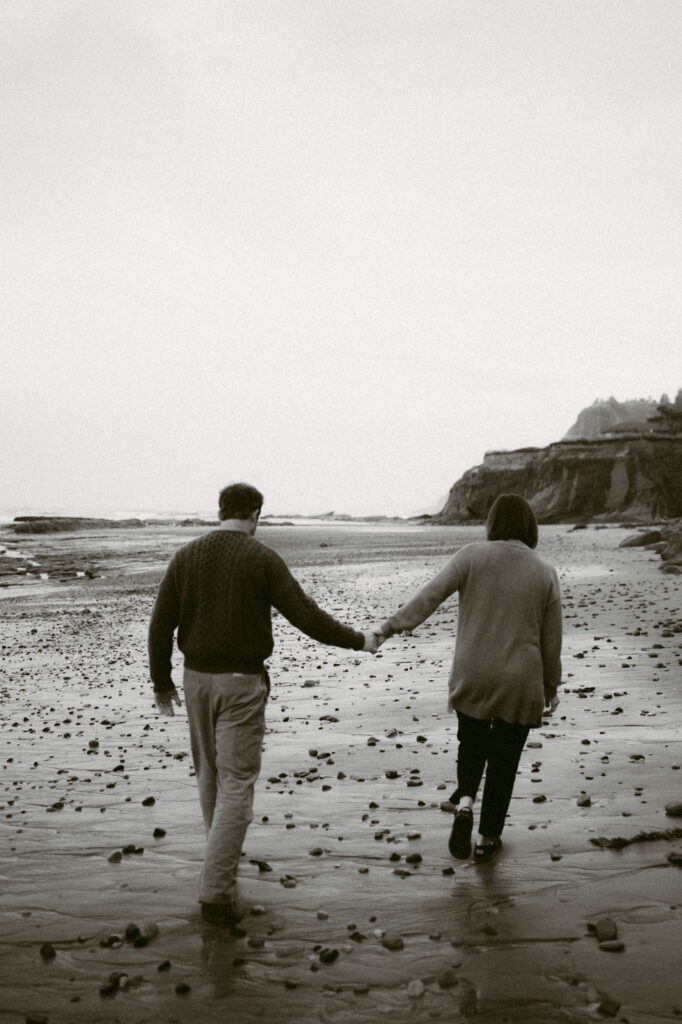 A black and white image of a man and woman walking hand in hand away from the camera.