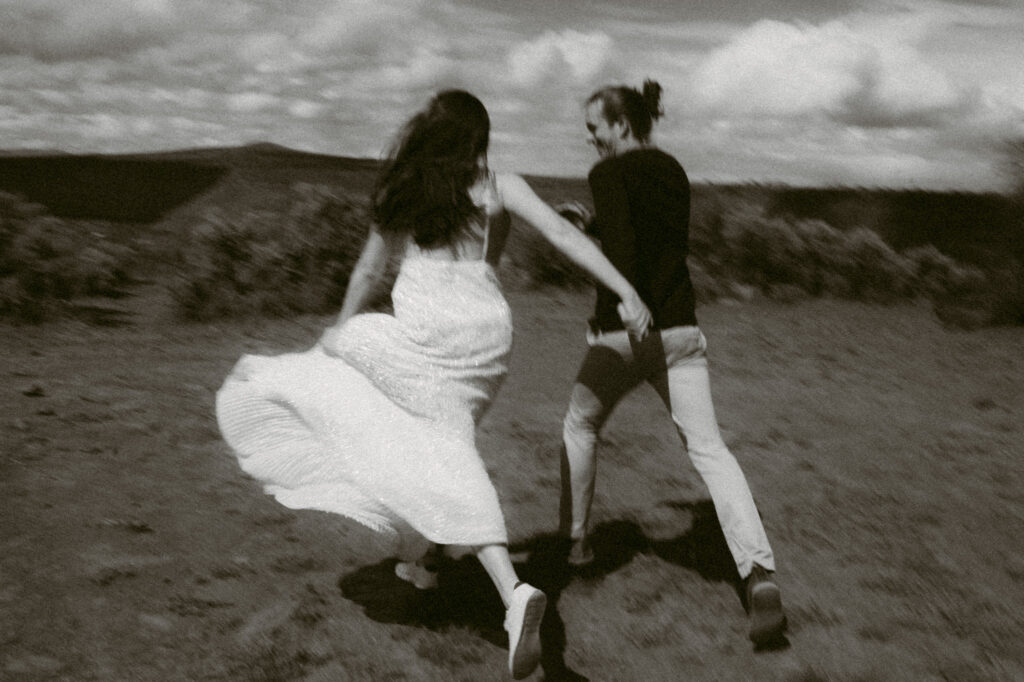 A blurry black and white image of a man and woman, holding hands and running away from the camera.