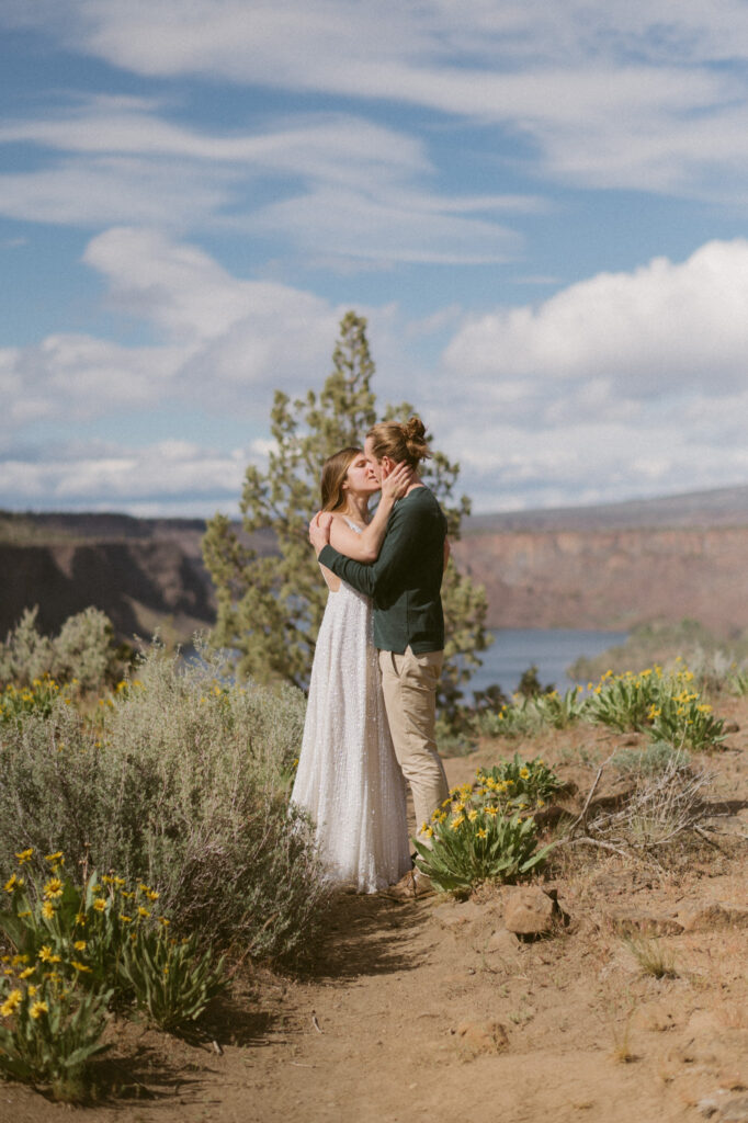 A man and woman stand amongst the wildflowers at Cove Palisades State park in Oregon, gently kissing.